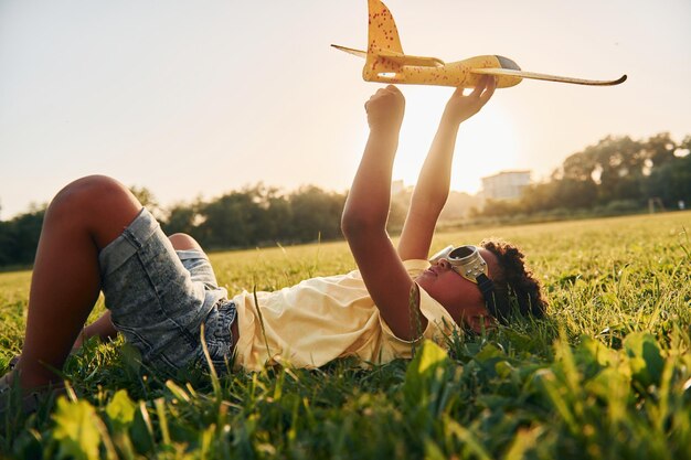 Boy with toy plane African american kid have fun in the field at summer daytime