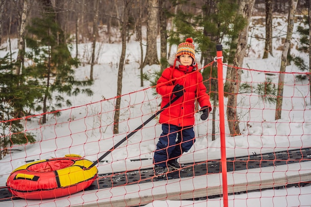 Boy with tubing rises on a travelator to the mountain Child having fun on snow tube Boy is riding a tubing Winter fun for children