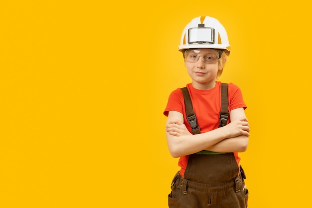 Boy in work overalls protective helmet and glasses on yellow background Choosing profession Copy space mock up