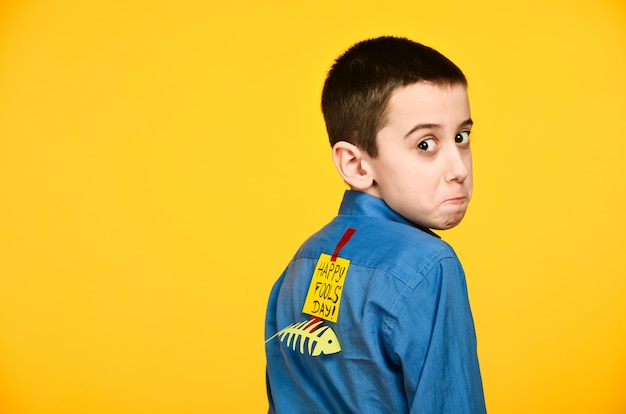 The boy on a yellow background in a blue shirt with a fish glued tape and a piece of paper on his back