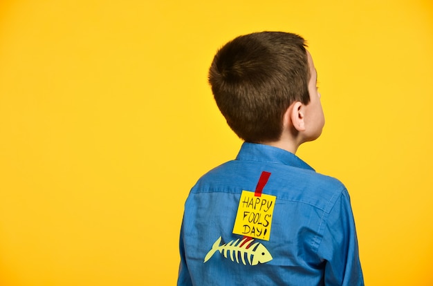 The boy on a yellow background in a blue shirt with a fish glued tape and a piece of paper on his back