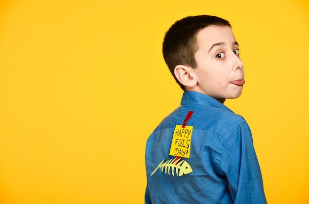 The boy on a yellow background in a blue shirt with a fish glued tape and a piece of paper on his back