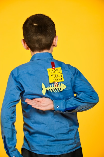 The boy on a yellow background in a blue shirt with a fish glued tape and a piece of paper on his back