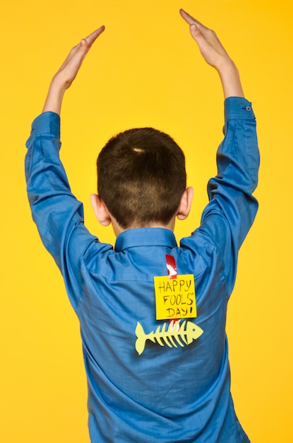 The boy on a yellow background in a blue shirt with a fish glued tape and a piece of paper on his back