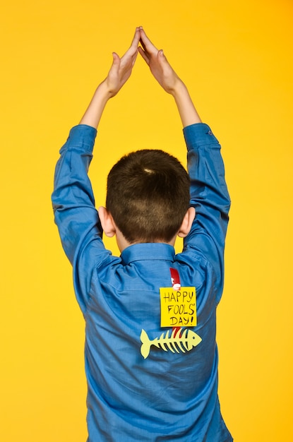 The boy on a yellow background in a blue shirt with a fish glued tape and a piece of paper on his back