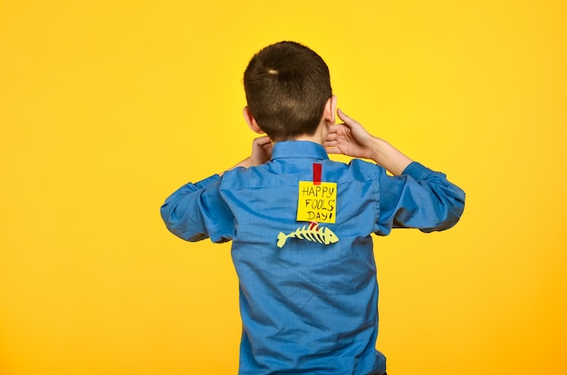 The boy on a yellow background in a blue shirt with a fish glued tape and a piece of paper on his back