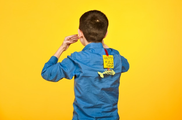 The boy on a yellow background in a blue shirt with a fish glued tape and a piece of paper on his back