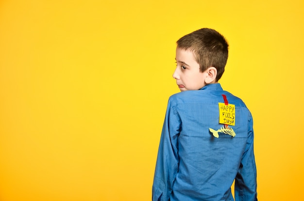 The boy on a yellow background in a blue shirt with a fish glued tape and a piece of paper on his back