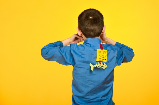 The boy on a yellow background in a blue shirt with a fish glued tape and a piece of paper on his back