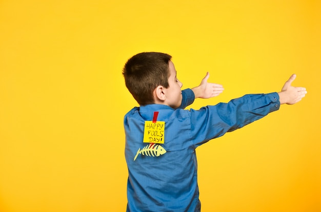 The boy on a yellow background in a blue shirt with a fish glued tape and a piece of paper on his back