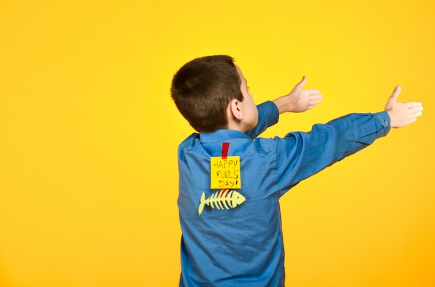 The boy on a yellow background in a blue shirt with a fish glued tape and a piece of paper on his back