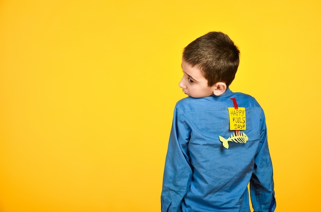 The boy on a yellow background in a blue shirt with a fish glued tape and a piece of paper on his back