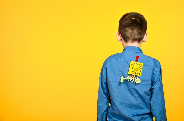 The boy on a yellow background in a blue shirt with a fish glued tape and a piece of paper on his back