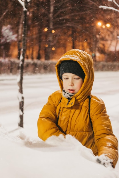 A boy in a yellow jacket plays with snow during a snowfall