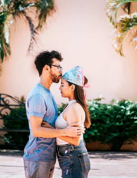 Boyfriend tenderly kissing his girlfriend forehead Man kissing his girlfriend forehead outside Cute couple embracing the boyfriend kisses the girl forehead Portrait of beautiful couple in love