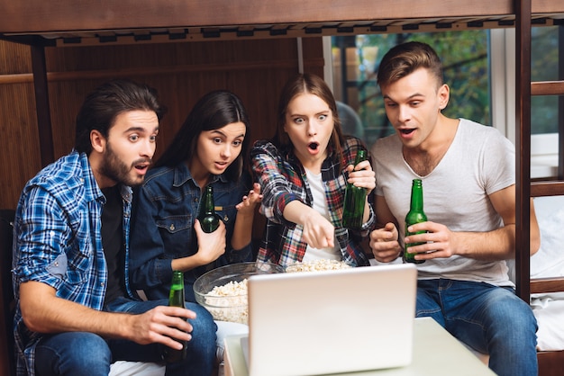 Boys and girls are watching movie on laptop with beer.