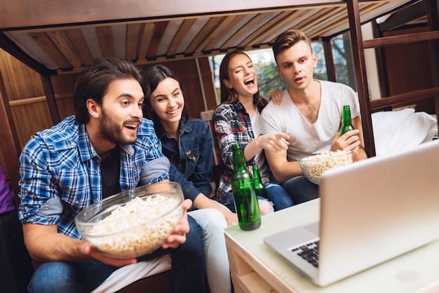 Boys and girls are watching movie on laptop with popcorn.