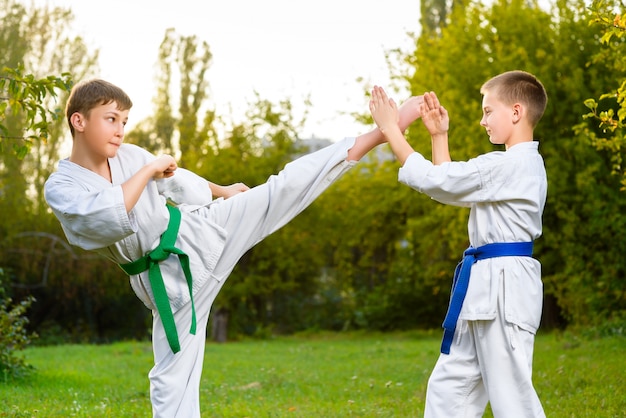 Boys in white kimono during training karate exercises at summer outdoors