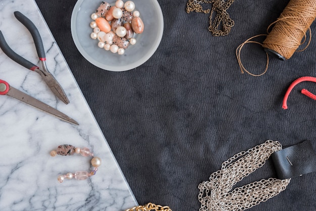 Bracelet made with the beads; chain; yarn spool; plier and scissor on textured backdrop