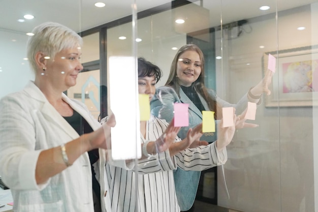 Brainstorming concept Group of happy creative business people looking at sticky notes on glass