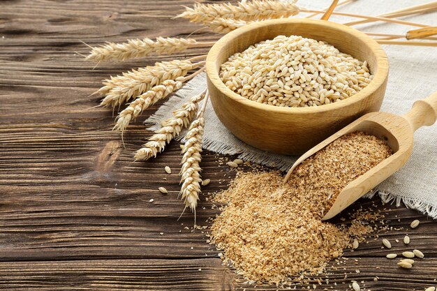 Bran, grain and wheat ears on a brown wooden table