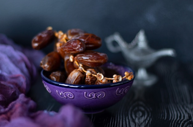 Branch of dried dates fruit in the purple plate on purple and black wood