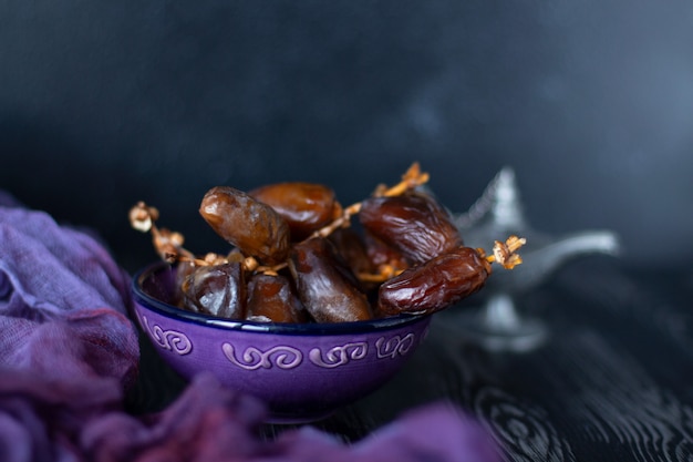 Branch of dried dates fruit in the purple plate on purple and black wood