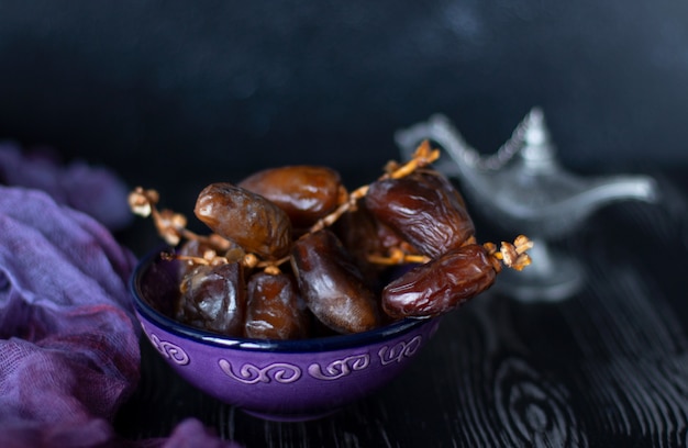 Branch of dried dates fruit in the purple plate on purple and black wood