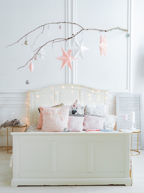 Branch with stars and garlands suspended scandinavian christmas interior with bed and tree