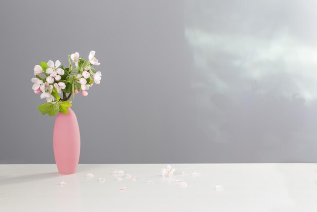 branches of apple tree with flowers in pink vase on white table