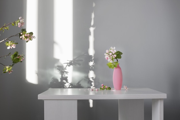 Branches of apple tree with flowers in pink vase on white table