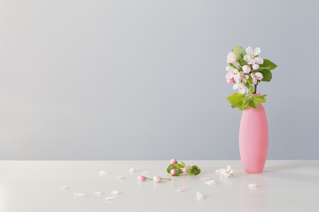 Branches of apple tree with flowers in pink vase on white table