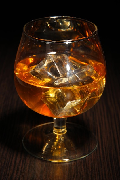 Brandy glass with ice on wooden background