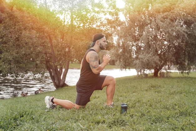 Brawny handsome bearded man sportsman with cap doing sport exercising outside in urban park with greenery Fitness healthy lifestyle concept