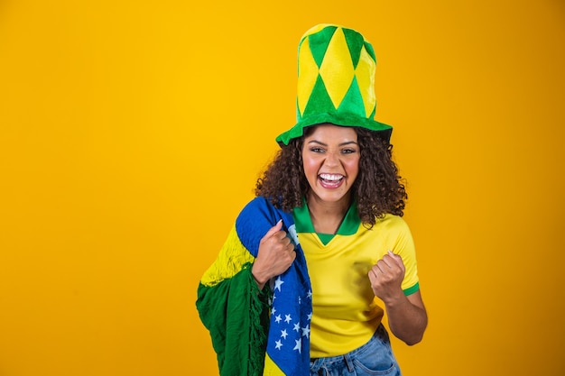 Brazil supporter. Brazilian curly hair woman fan celebrating on soccer, football match on yellow background. Brazil colors.