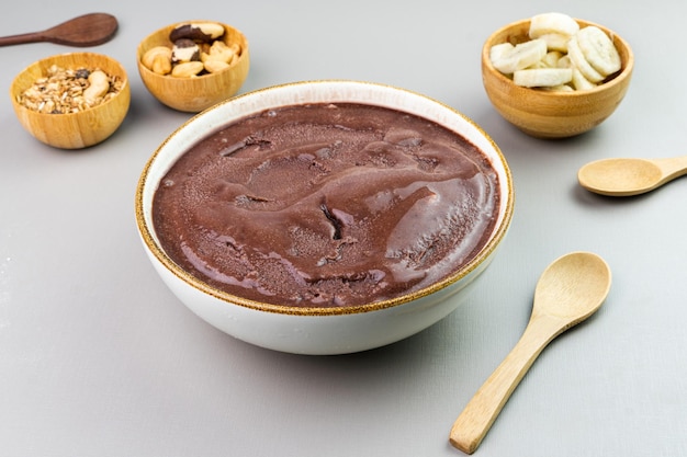 Brazilian acai in a white bowl additional banana granola and nuts in small bamboo bowls Cashew and Para nuts Top view Gray background Selective focus