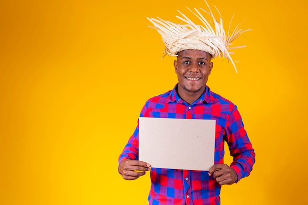 Brazilian afro man wearing typical clothes for the Festa Junina holding sign with space for text