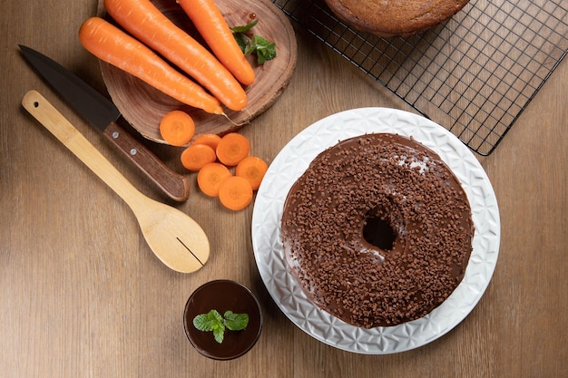 Brazilian carrot cake with chocolate frosting on wooden table with carrots in the background Top view