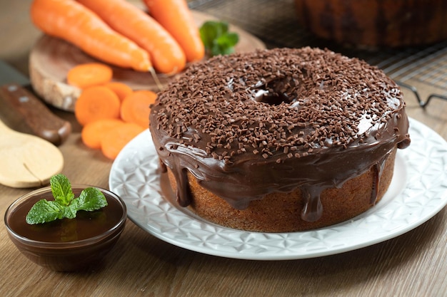 Brazilian carrot cake with chocolate frosting on wooden table with carrots in the background