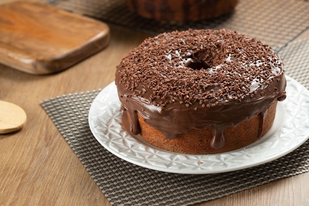 Brazilian carrot cake with chocolate frosting on wooden table with carrots in the background