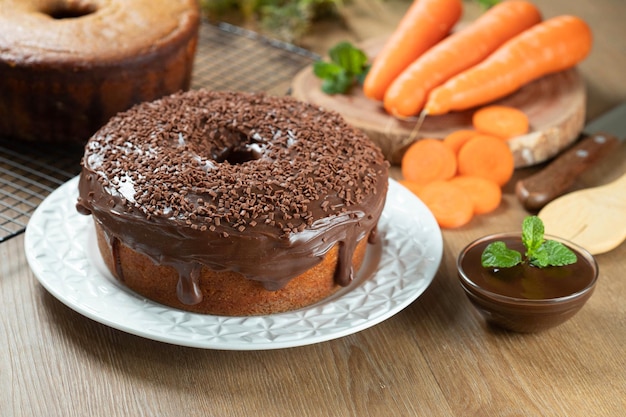 Brazilian carrot cake with chocolate frosting on wooden table with carrots in the background