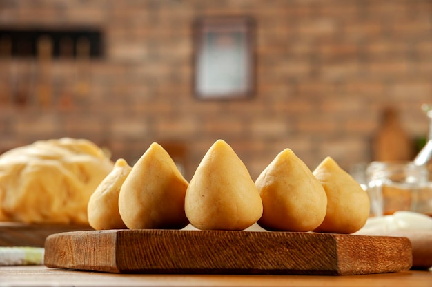 Brazilian chiken croquette coxinha de frango on a wooden table and a bricks kitchen background