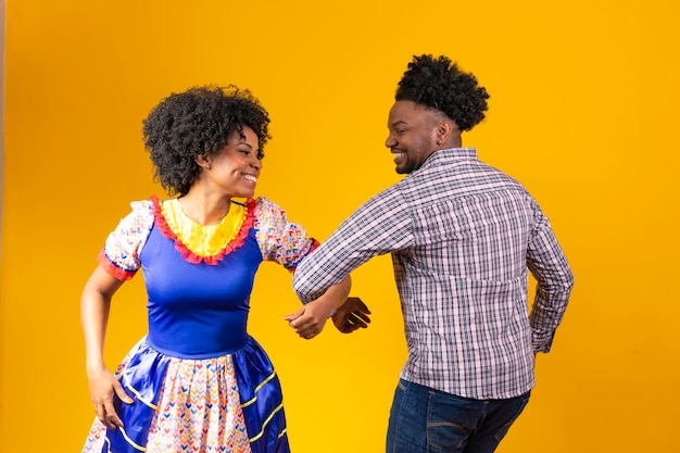 Brazilian couple wearing traditional clothes for Festa Junina dancing on yellow background