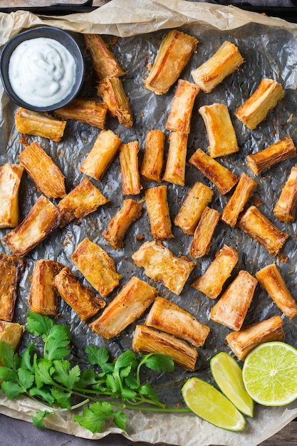 Brazilian cuisine food, latin snack. Fried yucca, yuca, cassava, manioca sticks with cilantro sauce. Top view flat lay background