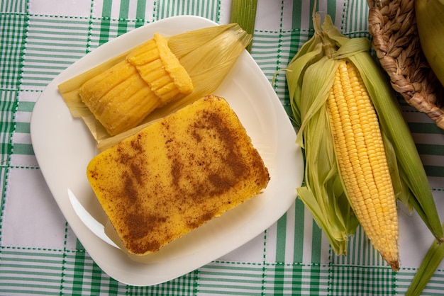 Brazilian Cural candy corn and pamonha corn on the cob arranged on a table with a green and white tablecloth dark background selective focus