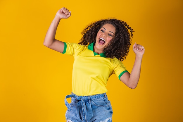 Brazilian fan. Jumping to celebrate, Brazilian fan celebrating football or soccer game on yellow background. Colors of Brazil.