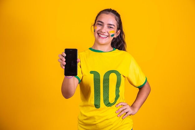 Brazilian fan portrait Brazilian fan showing her cell phone dressed as a football fan or football game on yellow background Colors of BrazilWorld Cup