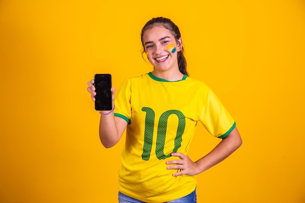 Brazilian fan portrait Brazilian fan showing her cell phone dressed as a football fan or football game on yellow background Colors of BrazilWorld Cup