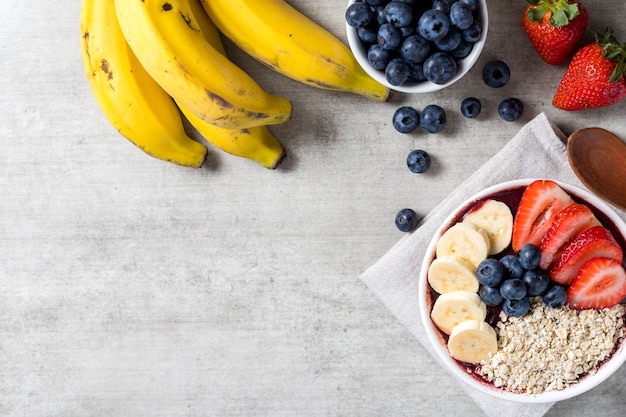 Brazilian frozen and acai berry ice cream bowl with strawberries, bananas, blueberry and oatmeal flakes. with fruits on wooden background. Summer menu top view. close up