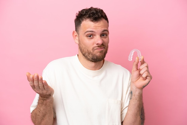 Brazilian man holding invisible braces making doubts gesture while lifting the shoulders